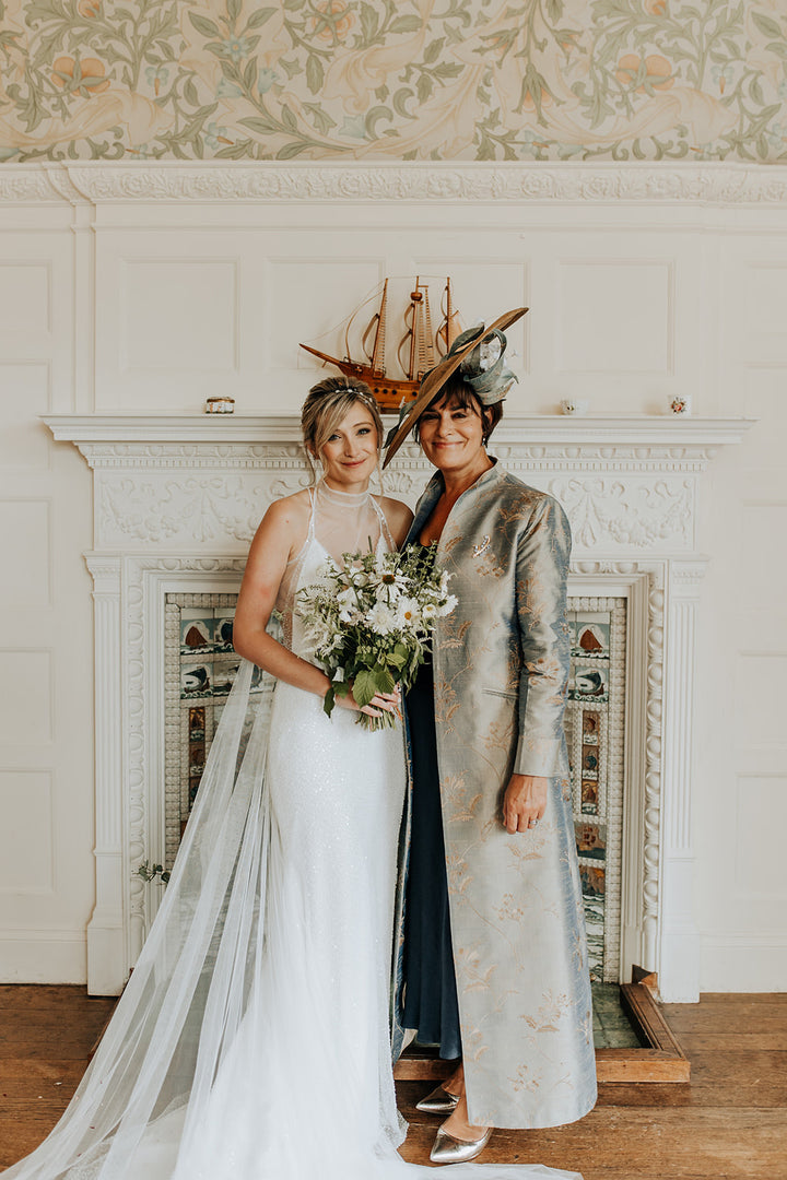 mother of the bride in her long silk maxi coat standing next to the bride who is wearing white dress. 