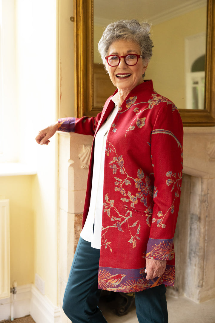 Lady in an open jacket that is red with green and purple flowers and birds. Jacket that is perfect for mature ladies and can be worn for events but also casually. 