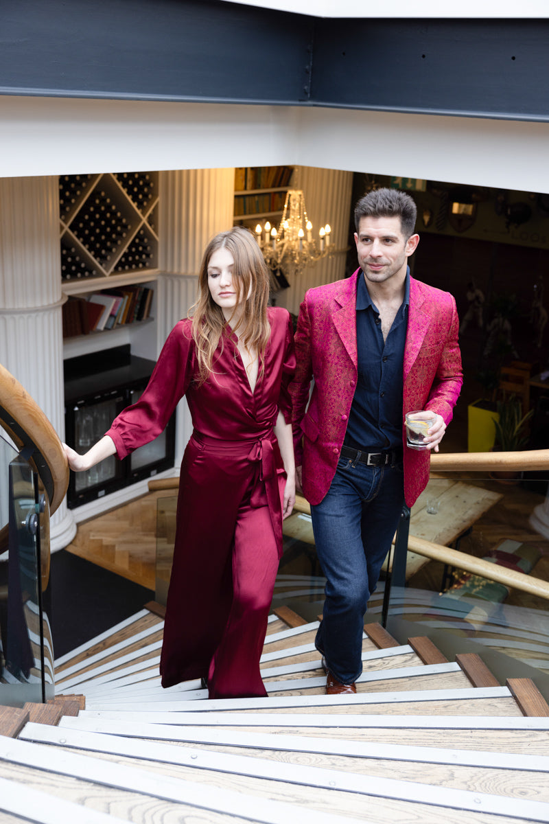 man walking up the stairs wearing striking dark pink silk jacket with a women in cherry jumpsuit