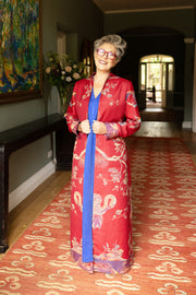 Older lady in a full length red coat. Long elegant cashmere coat with yellow and purple flowers and birds. Blue kaftan underneath it making it the perfect outfit for the night at the opera. 