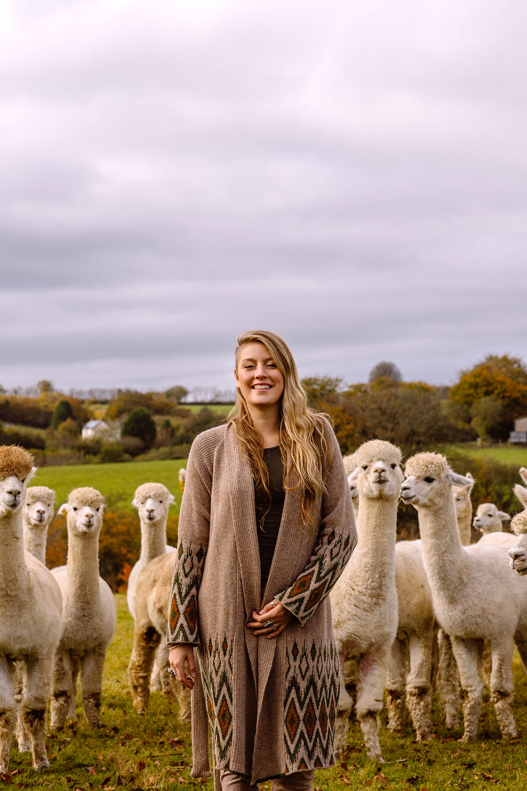 Young woman smiling, wearing long open cardigan. 